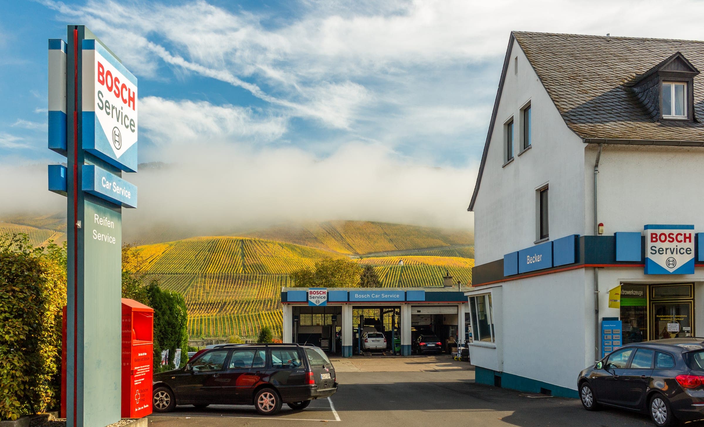 Werkstattgebäude der Ing. Leo Becker GmbH mit Bosch-Service-Pylon, im Hintergrund die herbstlichen Weinberge der Mosel
