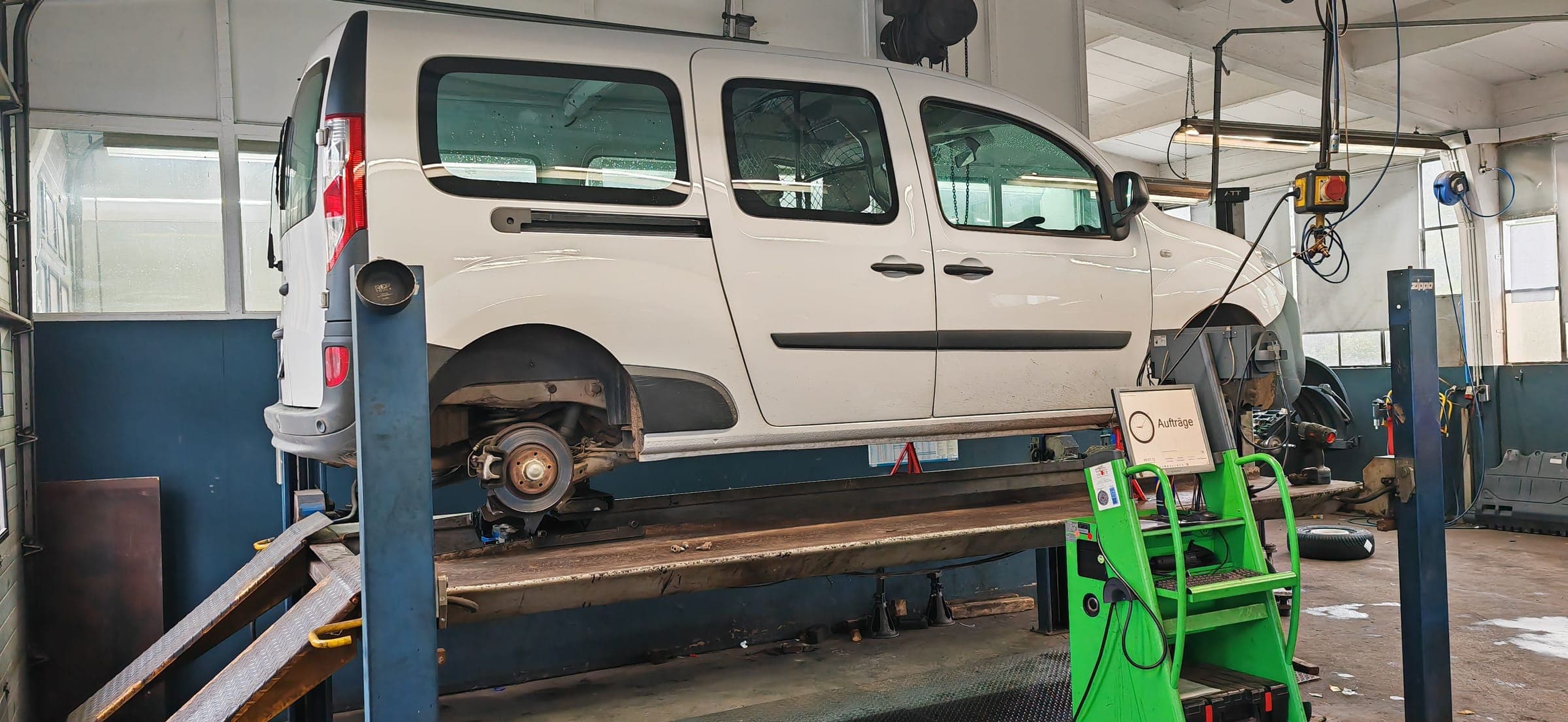 Ein Transporter auf der Vier-Säulen-Bühne, das Hinterrad abgenommen, Bremsscheibe und Sattel frei, davor der grüne Bosch-Prüfwagen