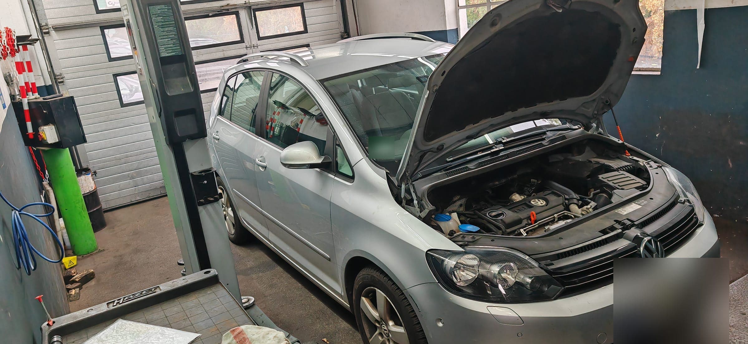 Ein VW Golf Plus mit geöffneter Motorhaube in der Werkstatt, daneben eine Zwei-Säulen-Hebebühne